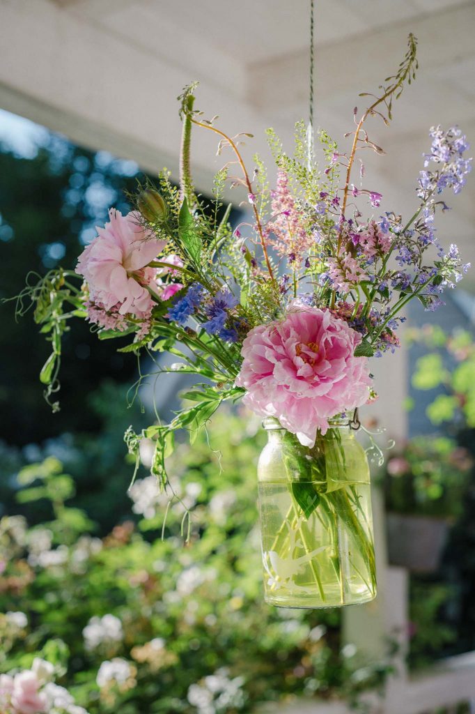 Hängende Glasvase mit Sommerblumen als Terrassendekoration